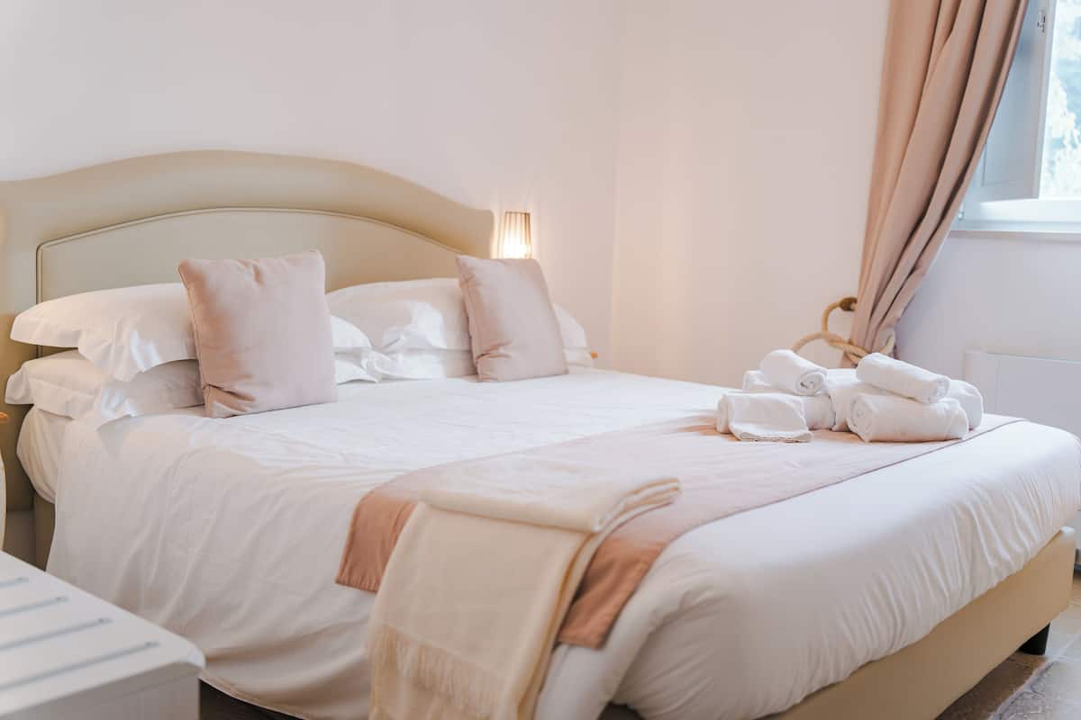A neatly made bed with pillows, a blanket, and rolled towels.