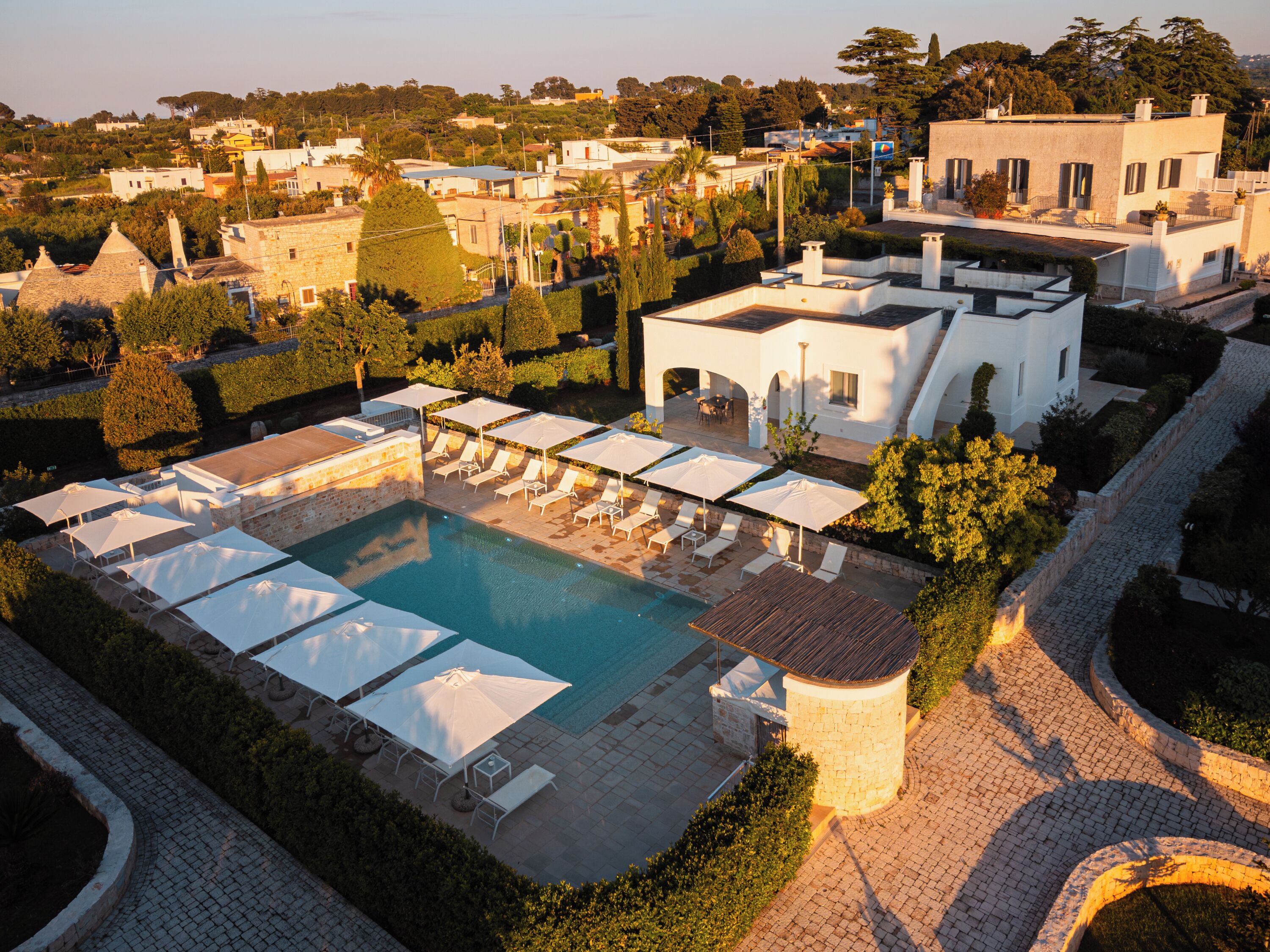 An aerial view of a resort with a swimming pool, sun loungers, and umbrellas.