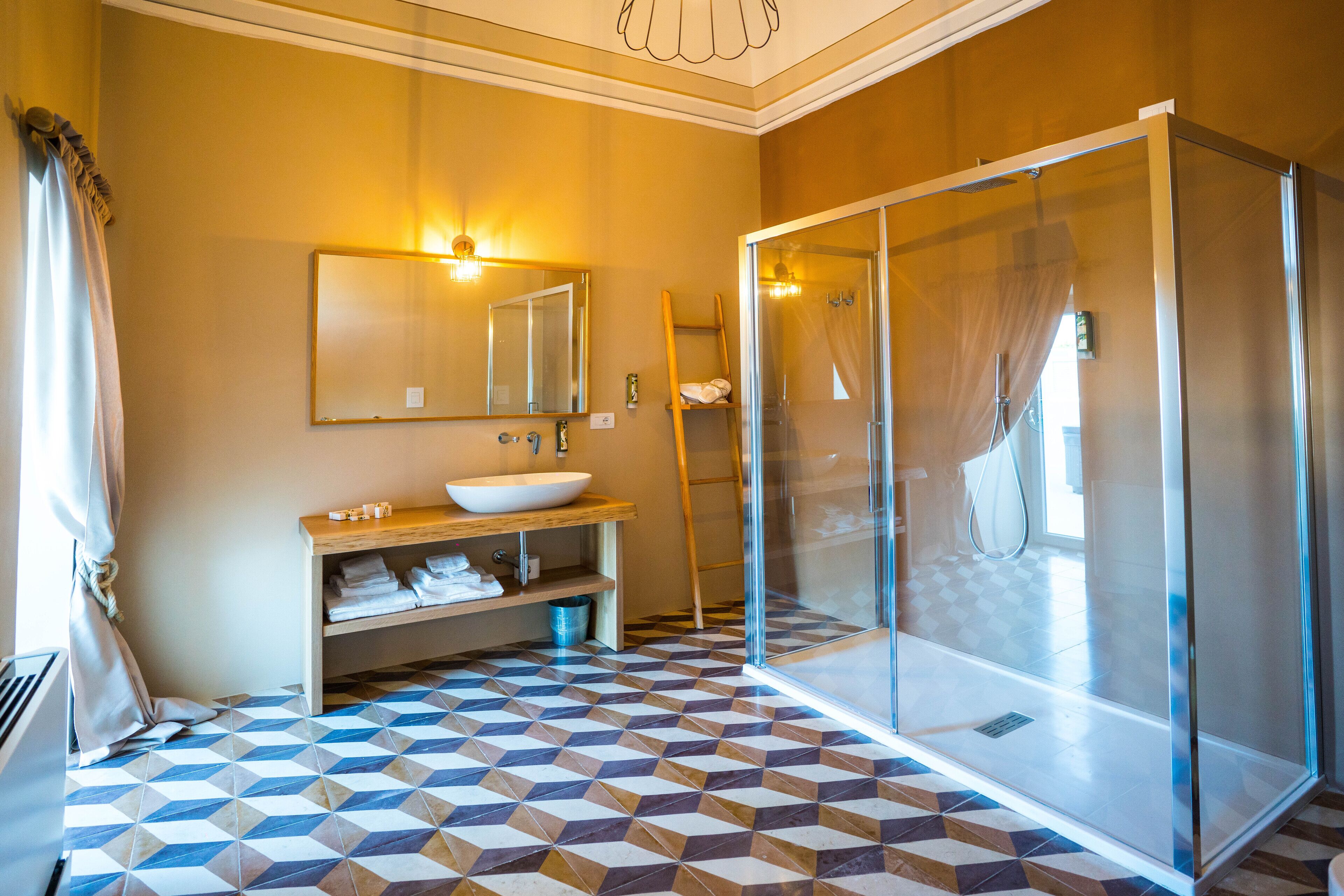 A bathroom with a geometric patterned floor, a large mirror, a sink with a wooden vanity, and a glass-enclosed shower area.