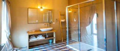 A bathroom with a geometric patterned floor, a large mirror, a sink with a wooden vanity, and a glass-enclosed shower area.