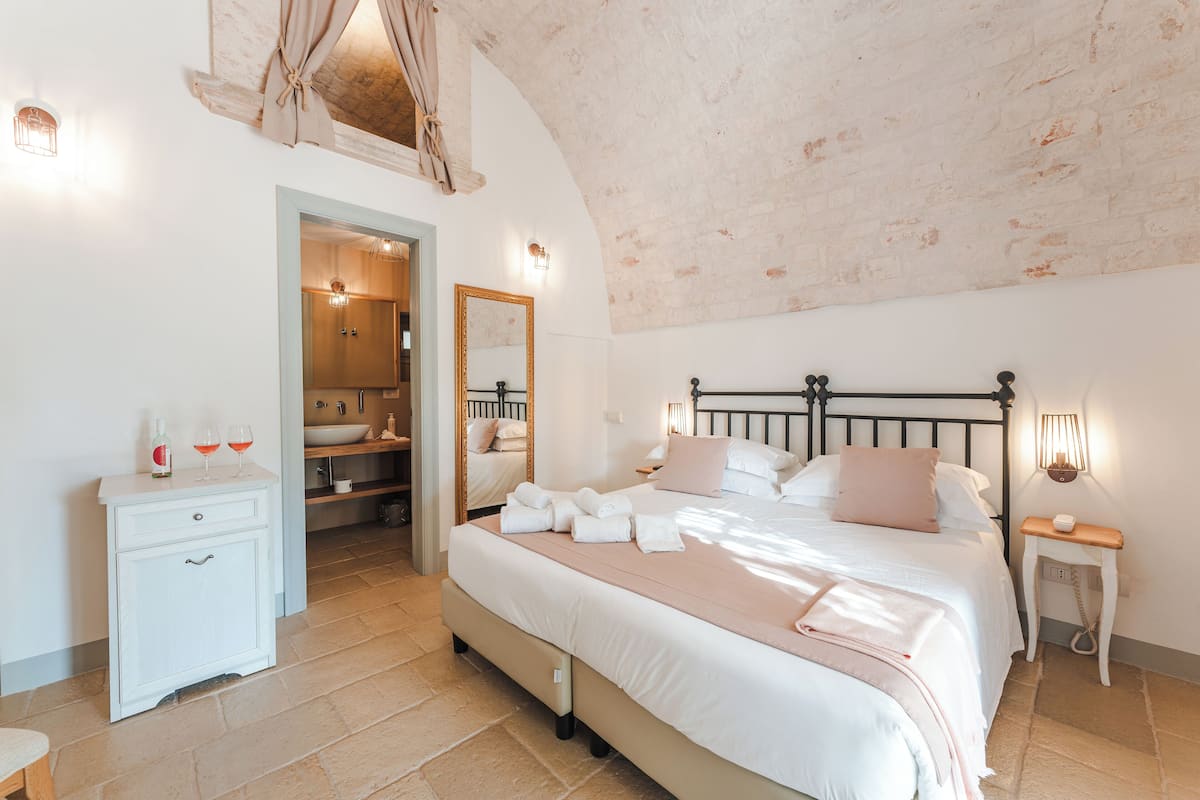A bedroom with a large bed, a bedside table, a nightstand, a wardrobe, and a bathroom visible through an open door.