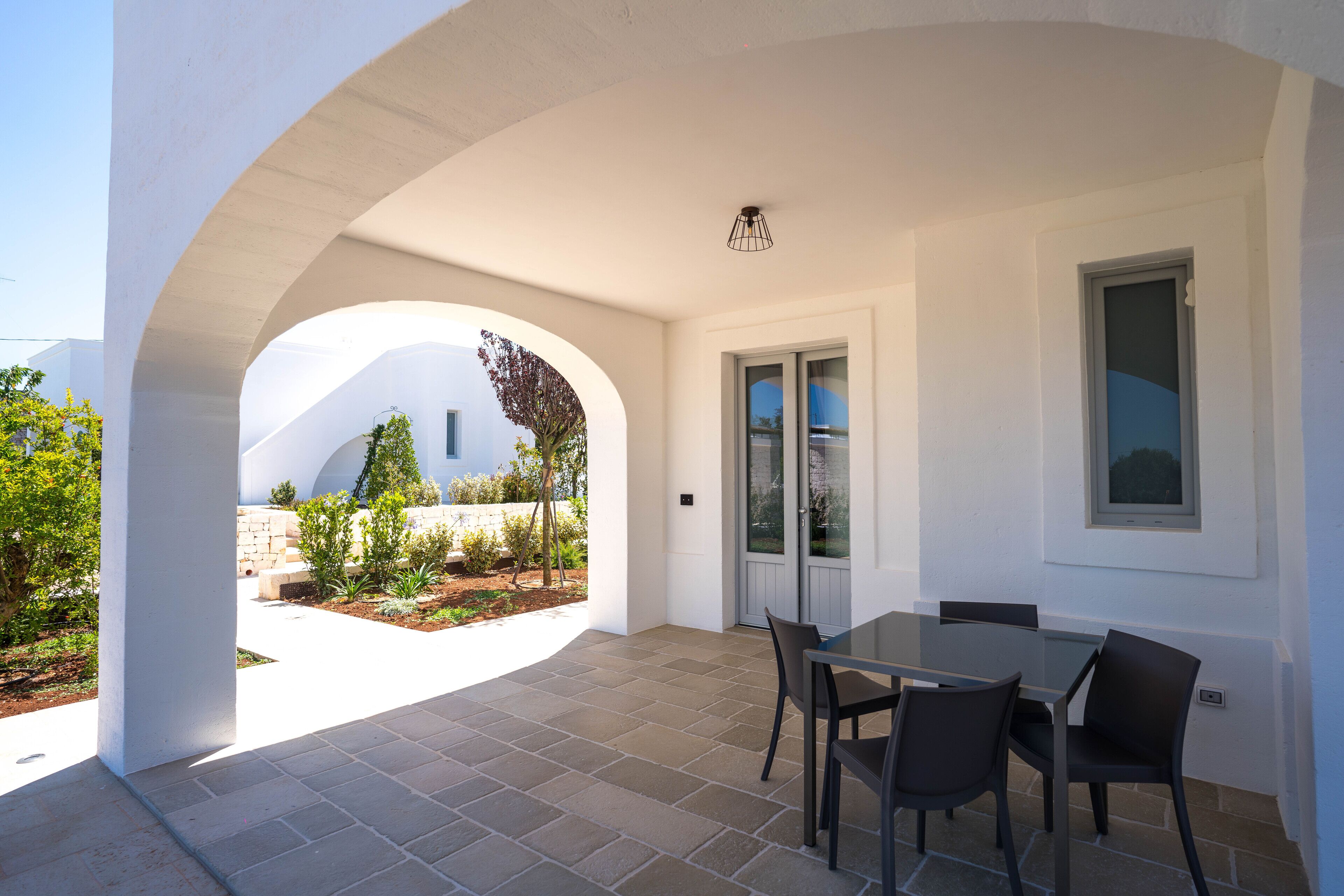 Un patio couvert avec une table et des chaises, une porte donnant sur l’extérieur et une vue sur un jardin.