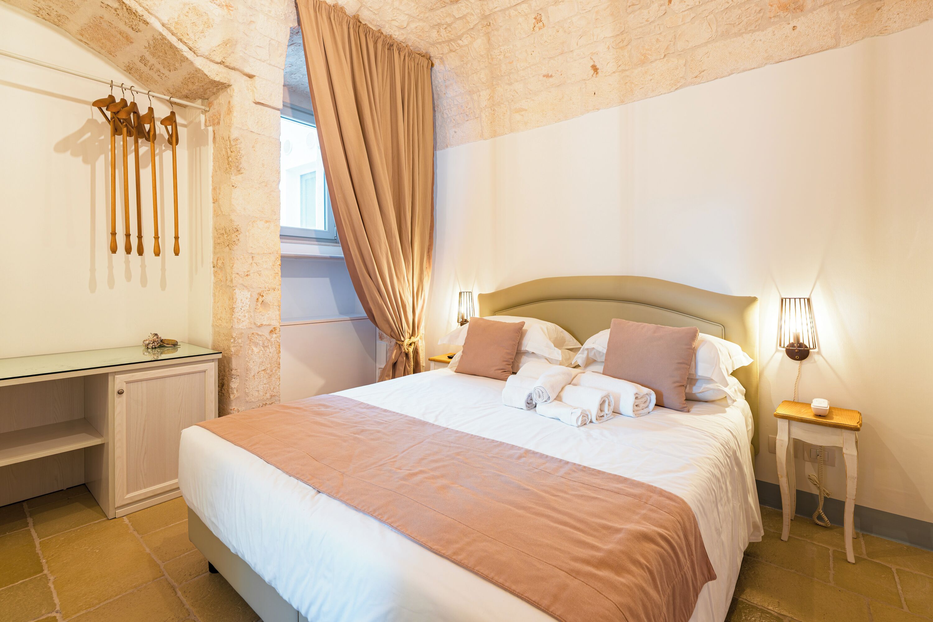Un lit bien fait, avec des oreillers et une couverture, une table de chevet avec une lampe, un miroir et une fenêtre avec des rideaux.