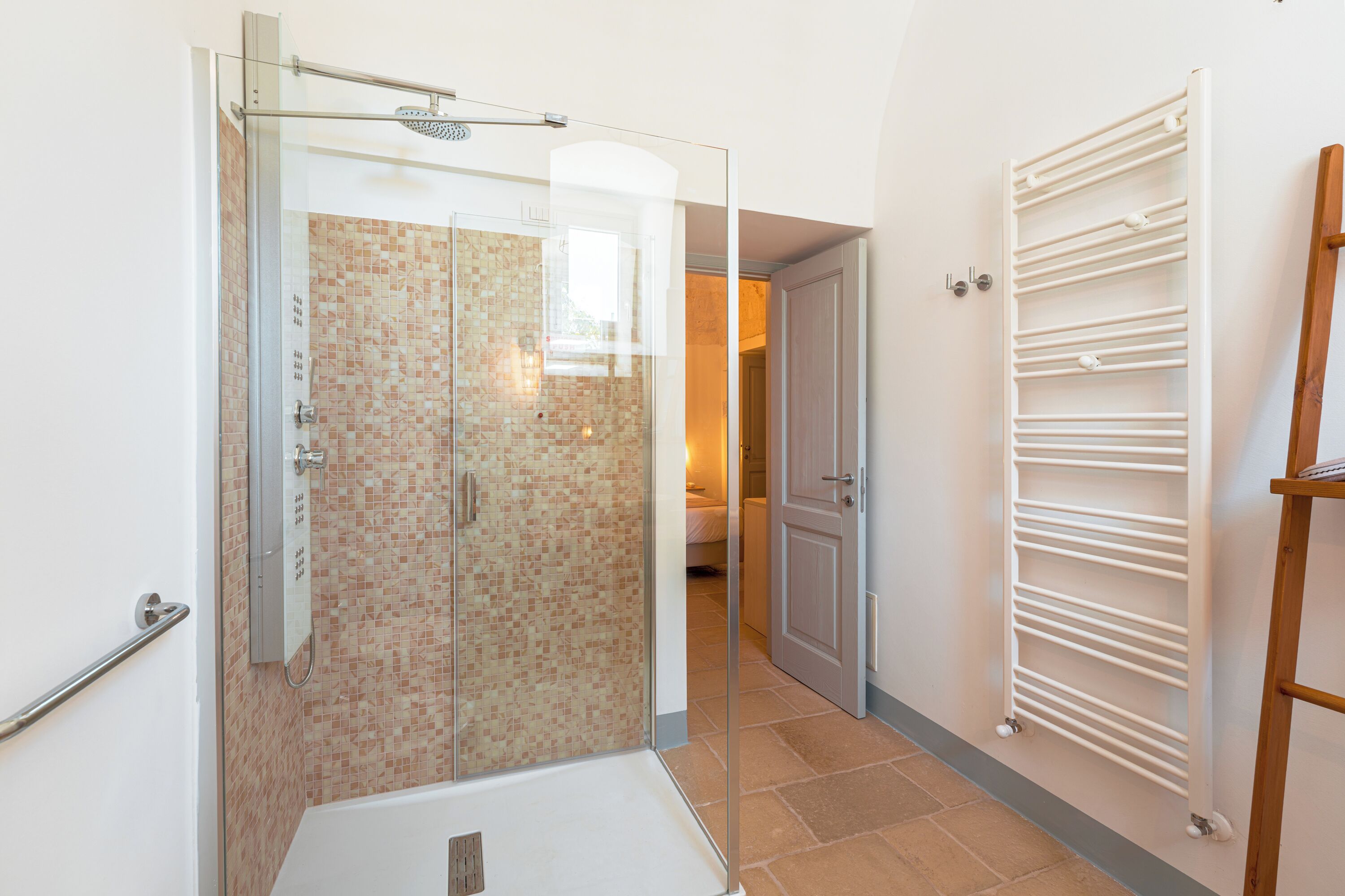 A shower with a glass door, a tiled shower area, and a white towel rack.