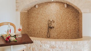 Un baño con pared revestida de mosaicos, una bañera y una mesa de madera con una copa de vino y flores.