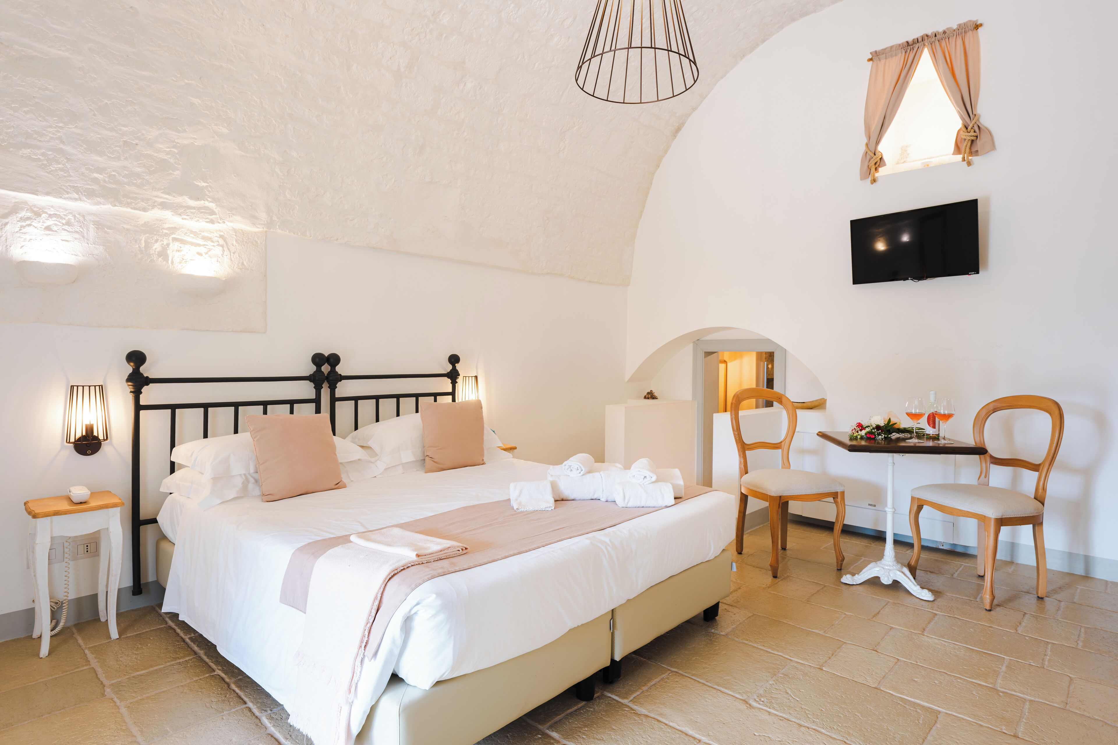 A bedroom with a bed, bedside tables, a TV, and a small table with drinks.