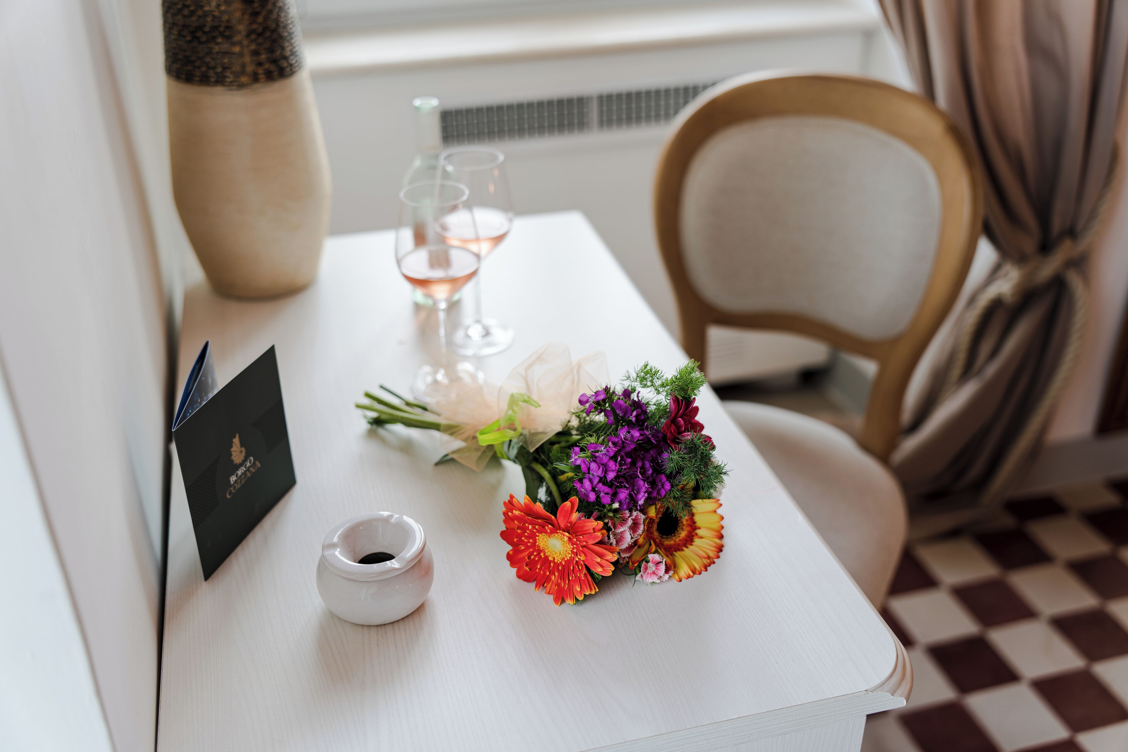 A neatly arranged table with a bouquet of flowers, a small white bowl, and a glass of wine.