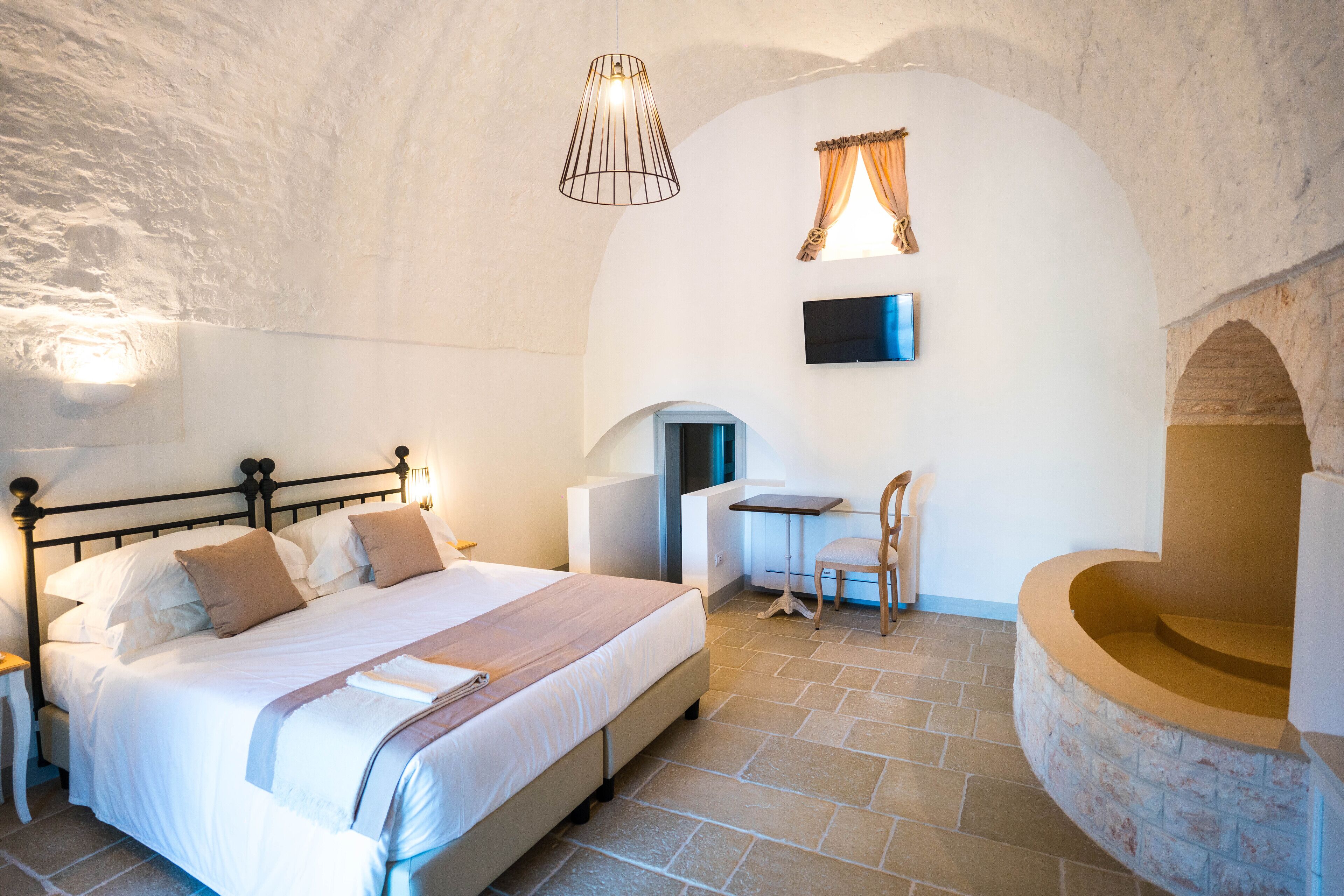 Ein Schlafzimmer mit einem Bett, einem Schreibtisch, einem Sessel, einem Fernseher und einem Kamin aus Stein.