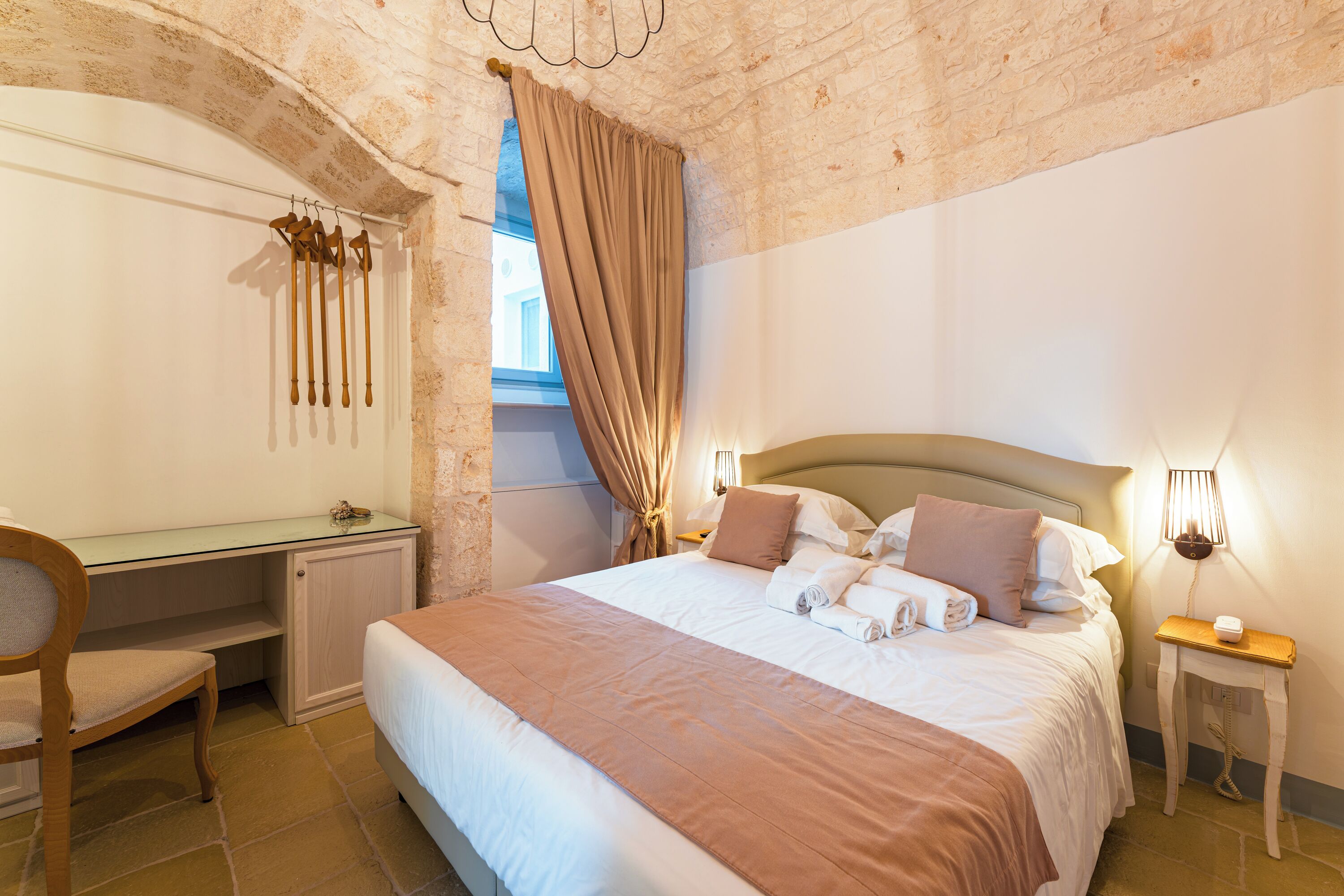 Un dormitorio con cama, escritorio, silla, ventana con cortinas y lámpara.