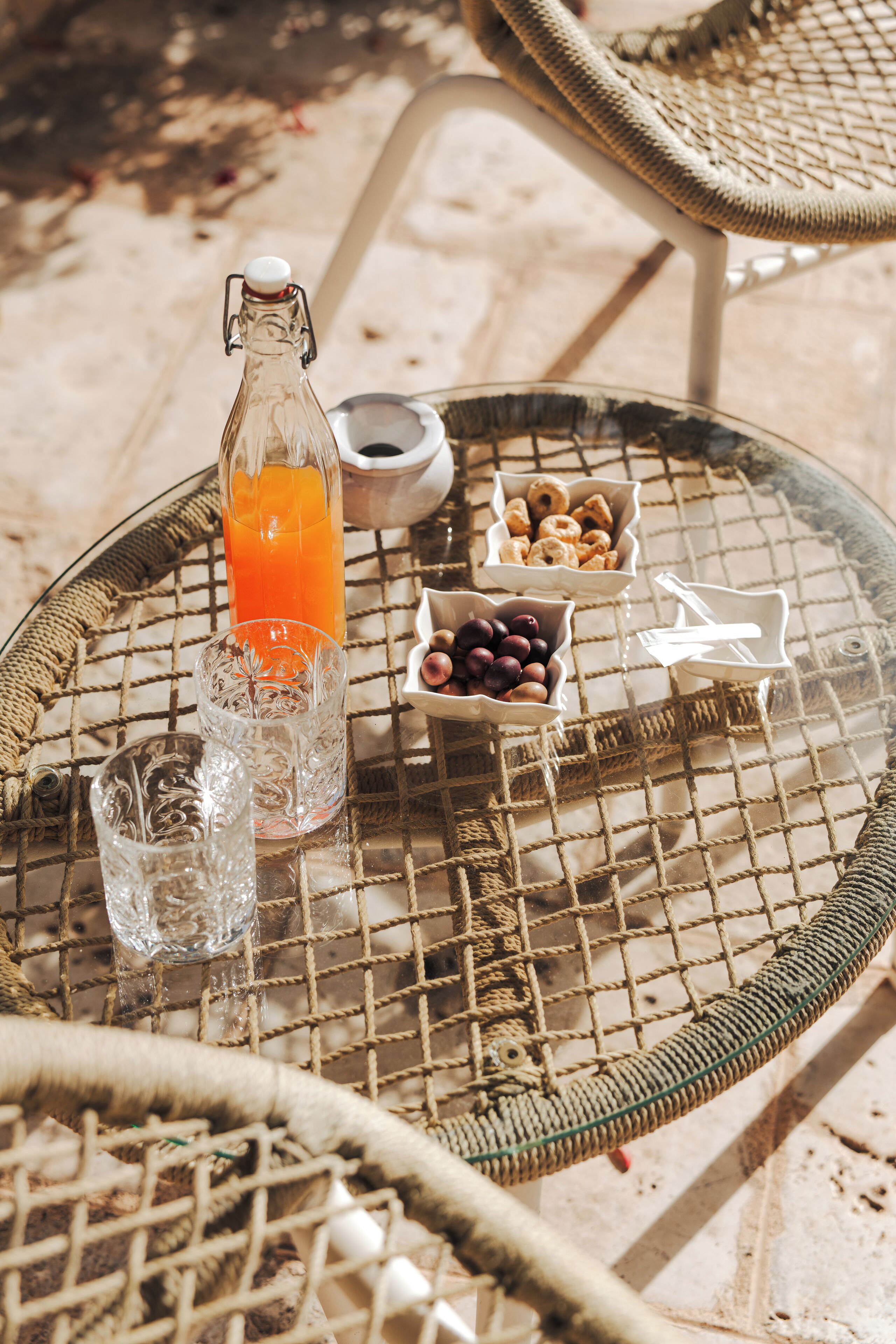 Une table en osier avec une bouteille de jus d’orange, un verre et des bols remplis de collations.