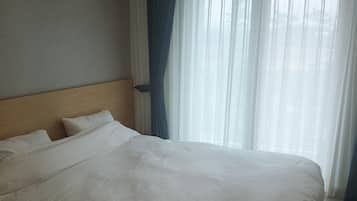 A hotel room with a large bed, a wooden headboard, and sheer curtains on the window.