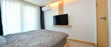 A bedroom with a bed, a mounted TV, and an air conditioning unit.