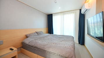 Een moderne hotelkamer met een groot bed, een nachtkastje, een airconditioning en een groot raam met gordijnen.