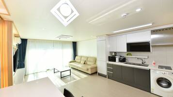 A modern kitchen with a washing machine, a sofa, and a dining area with a table and chairs.
