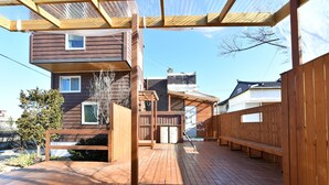 Una terraza de madera con una pérgola, un banco de madera y una mesa pequeña.