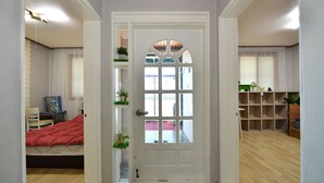 Habitación con cama, escritorio y una silla. Se aprecia una puerta con ventana y una estantería con plantas.