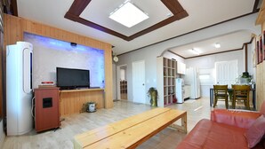 Una sala de estar con televisor, muebles de madera y una cocina al fondo.