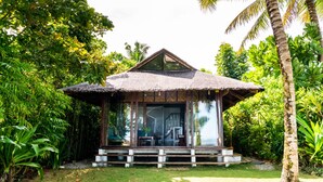 A thatched-roof structure with a glass enclosure, surrounded by lush greenery and palm trees. - Greenhouse Siargao (General Luna)
