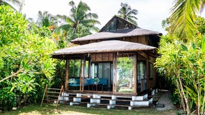 A wooden house with a thatched roof, surrounded by lush greenery and palm trees. - Greenhouse Siargao (General Luna)