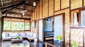 A spacious room with a wooden ceiling, large windows, a sofa set, a dining table, and a small plant. - Greenhouse Siargao (General Luna)