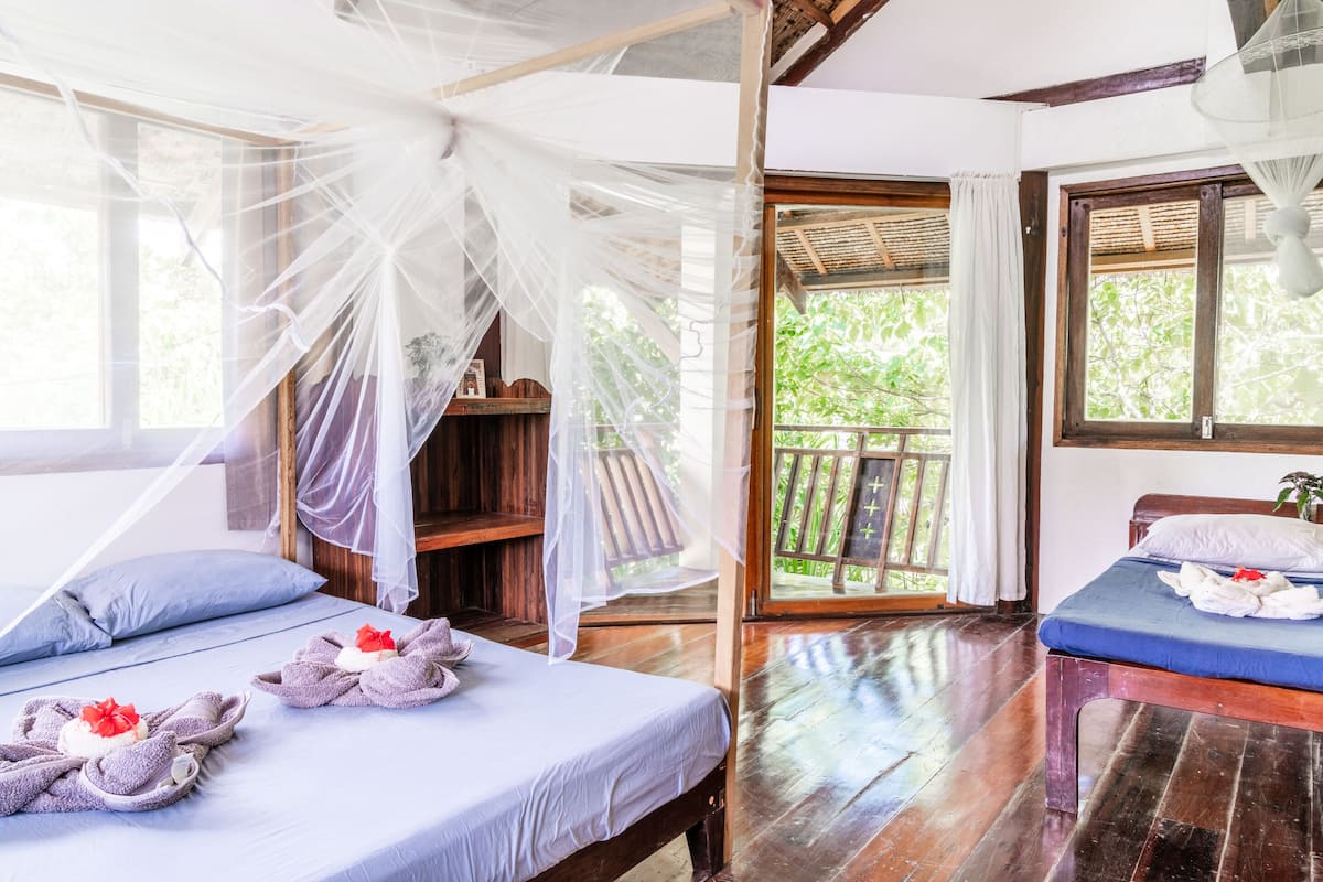 A room with two beds, one with a canopy and the other with a blue mattress. There are towels with flowers on the beds.