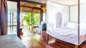 A room with a bed covered in a mosquito net, a wooden floor, a table with chairs, and a view of greenery outside. - Greenhouse Siargao (General Luna)
