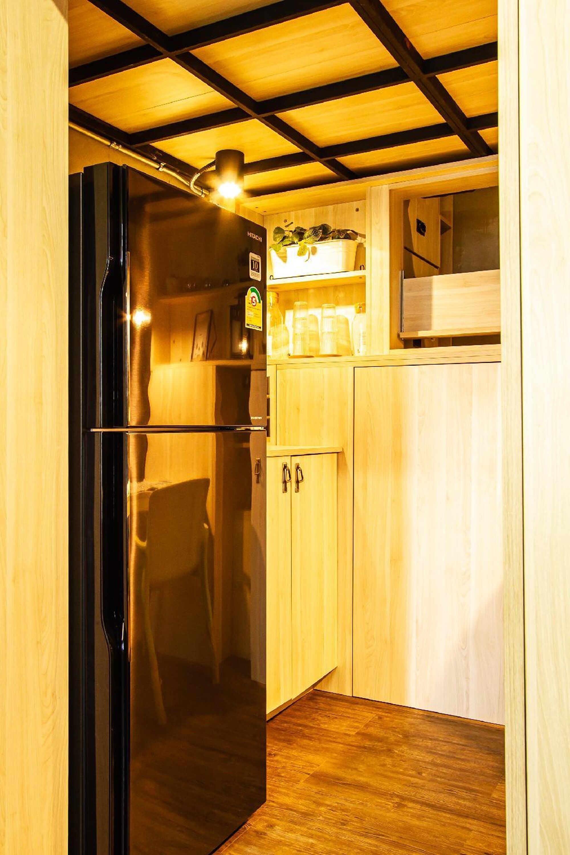 Une cuisine compacte avec des meubles de rangement en bois, un réfrigérateur noir et une étagère remplie de bocaux.