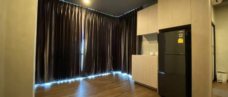 A modern kitchen with wooden flooring, a black refrigerator, and a curtain with LED lighting.
