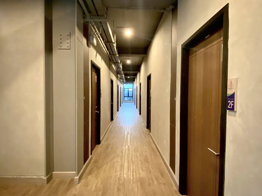 A long, narrow hallway with wooden flooring and doors on both sides, leading to a bright room at the end.