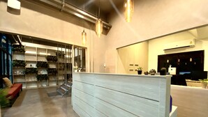 Un espace d’accueil moderne, doté d’un comptoir de réception en bois, d’un escalier avec une rampe en verre et d’un climatiseur fixé au mur.