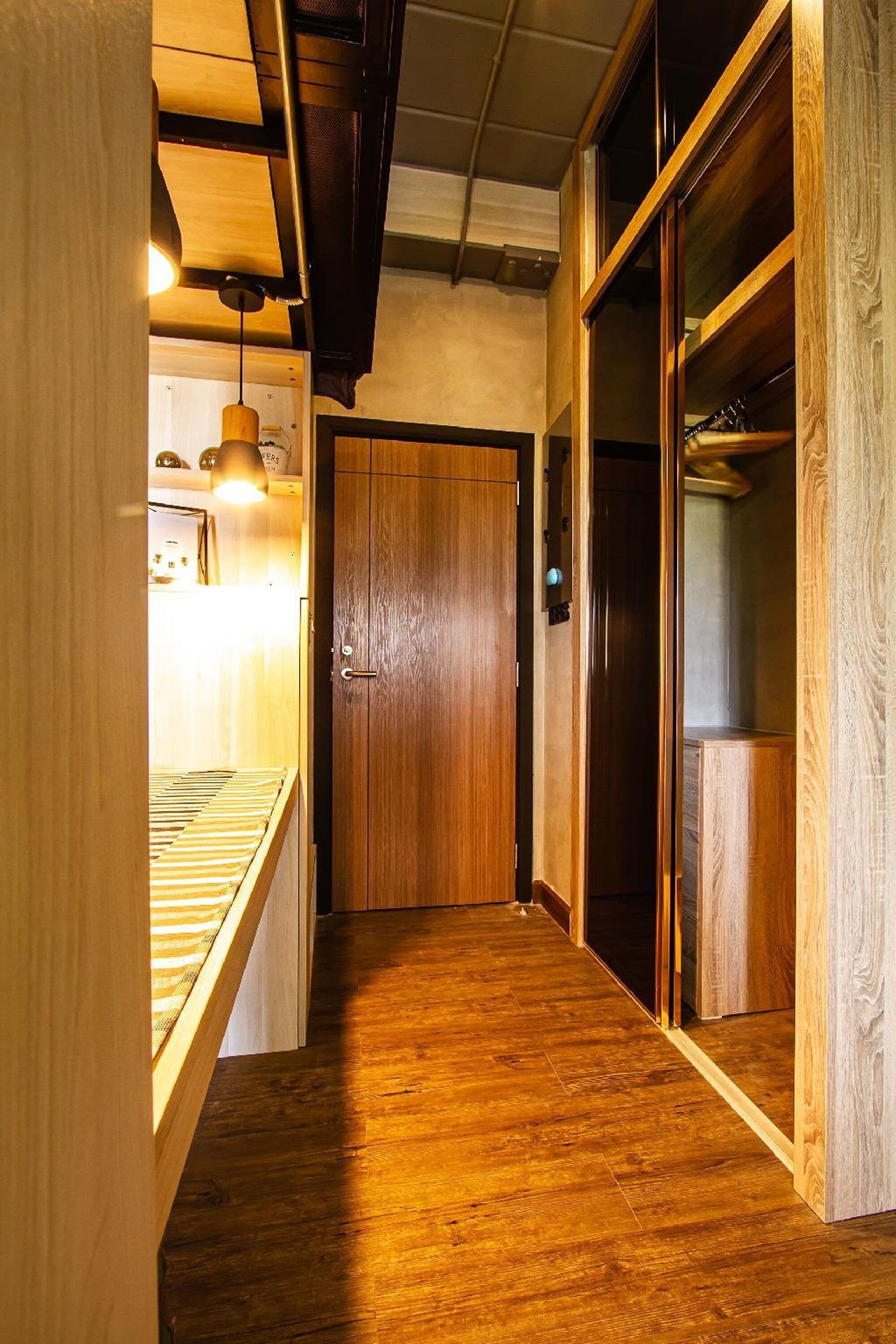 Un pasillo estrecho con suelo de madera y una puerta de madera al final.