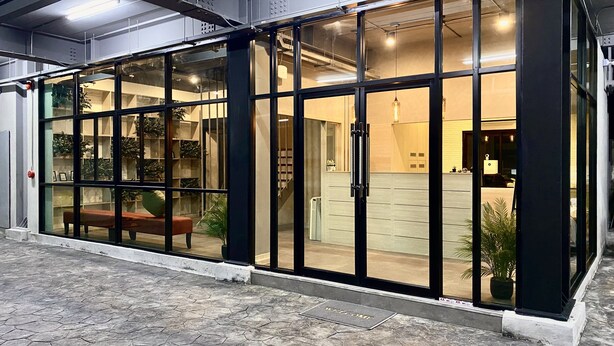 Un bâtiment moderne doté de grandes portes vitrées, d’un banc à l’extérieur et d’un paillasson à l’entrée.