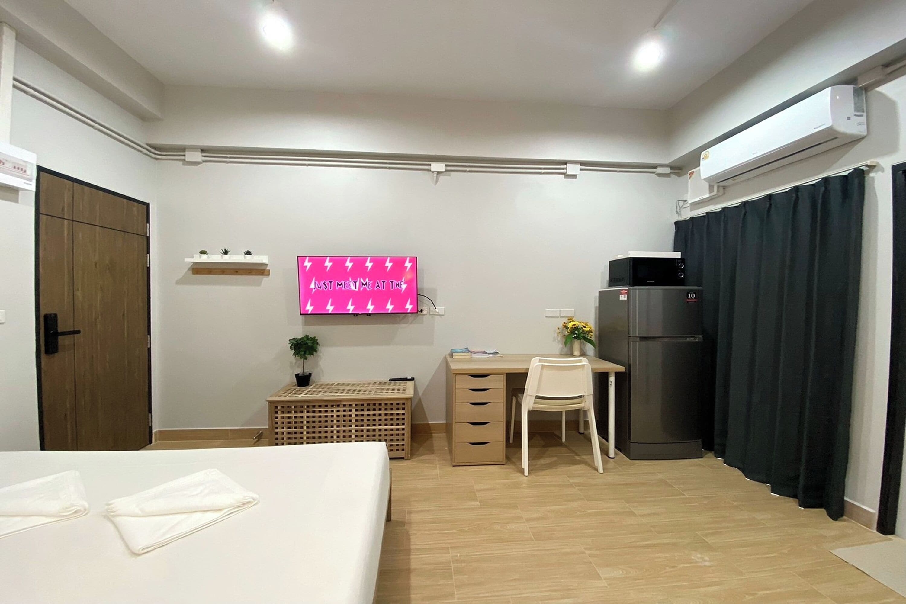 Habitació senzilla amb llit, escriptori, cadira, taula petita, nevera, televisió i armari.