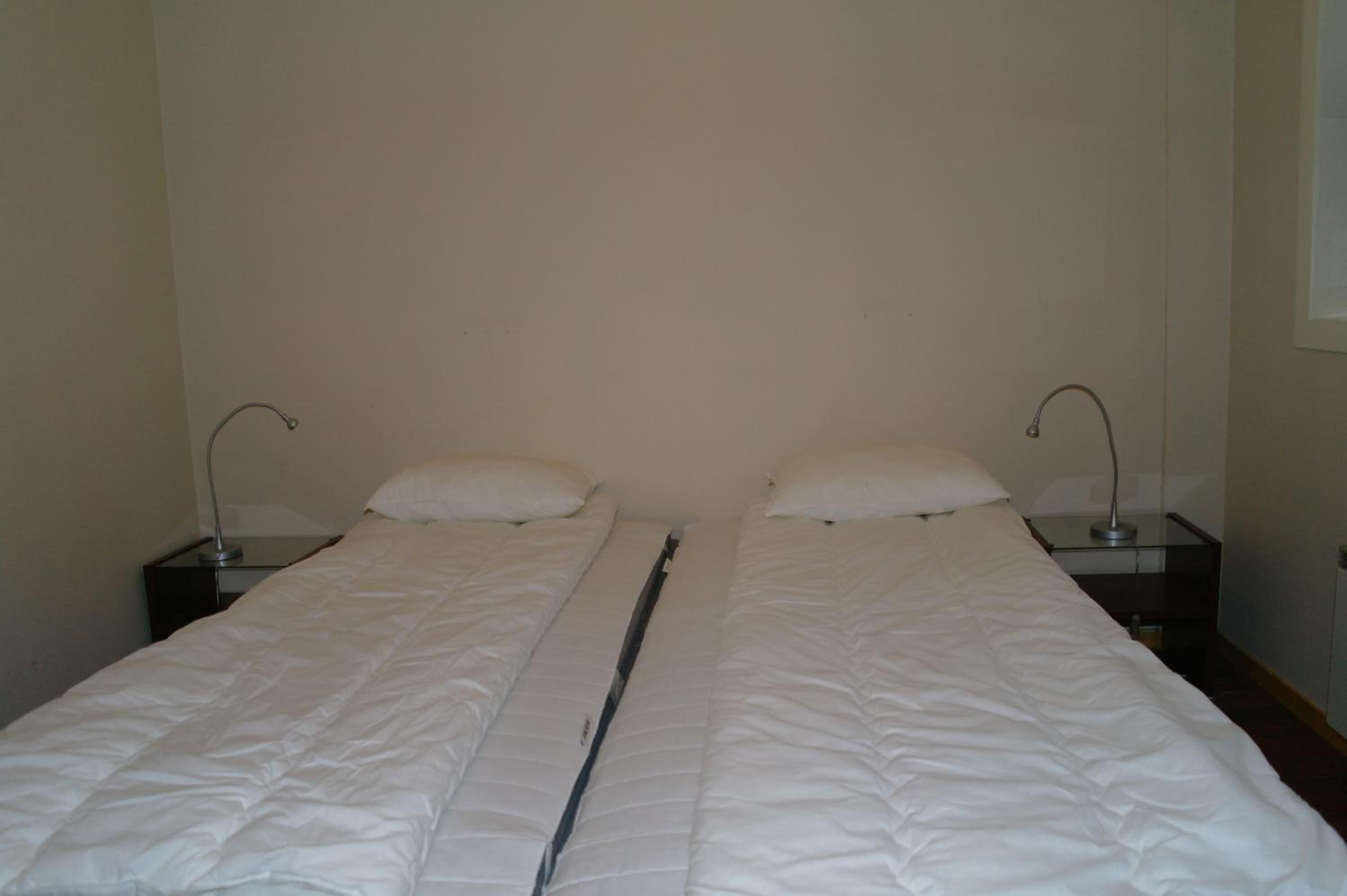 Ein Doppelbett mit weißer Bettwäsche, zwei Nachttische mit Lampen und eine schlichte Wand.