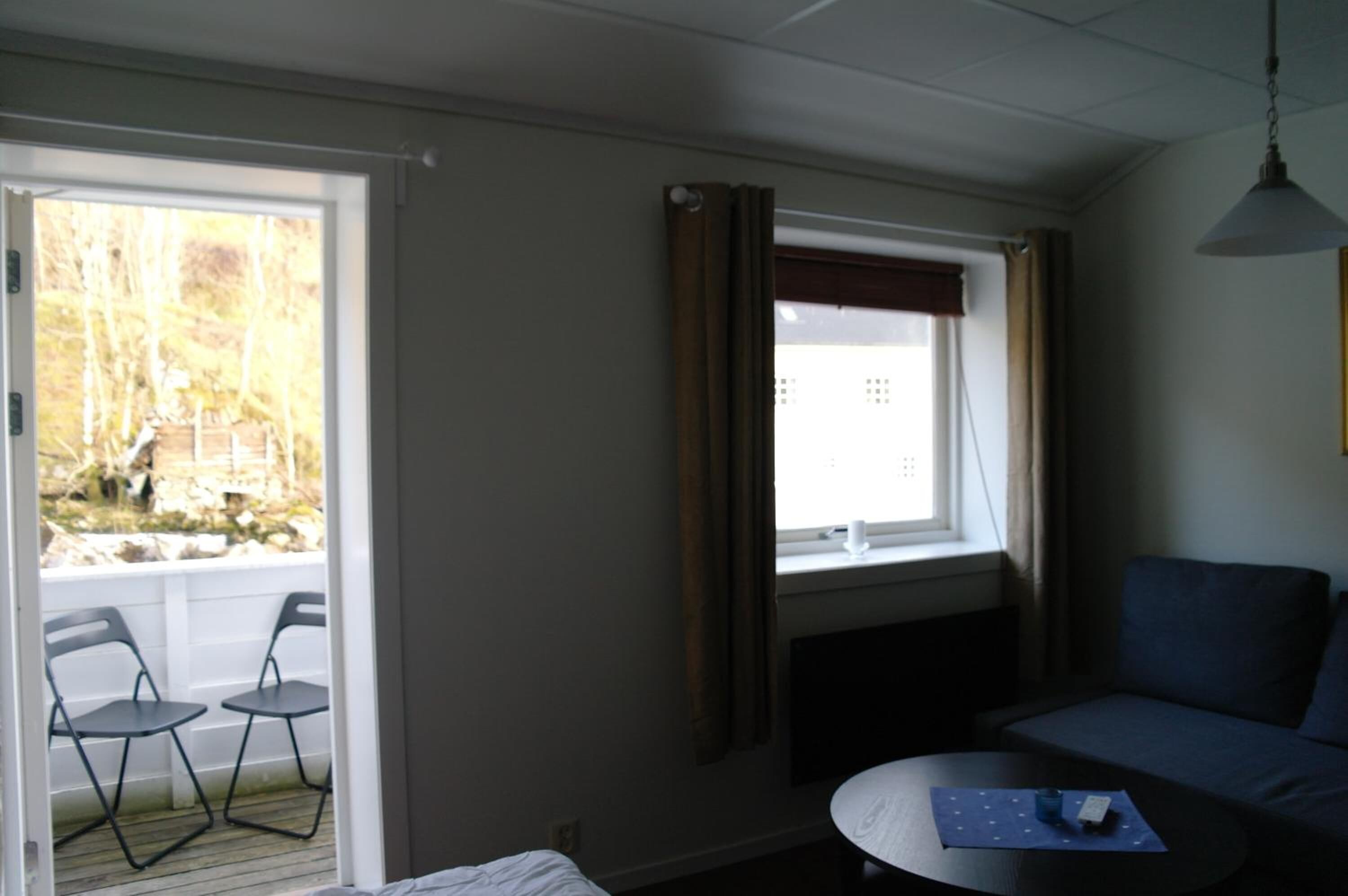 A room with a sofa, a table, and a window with curtains. There is a view of trees outside.