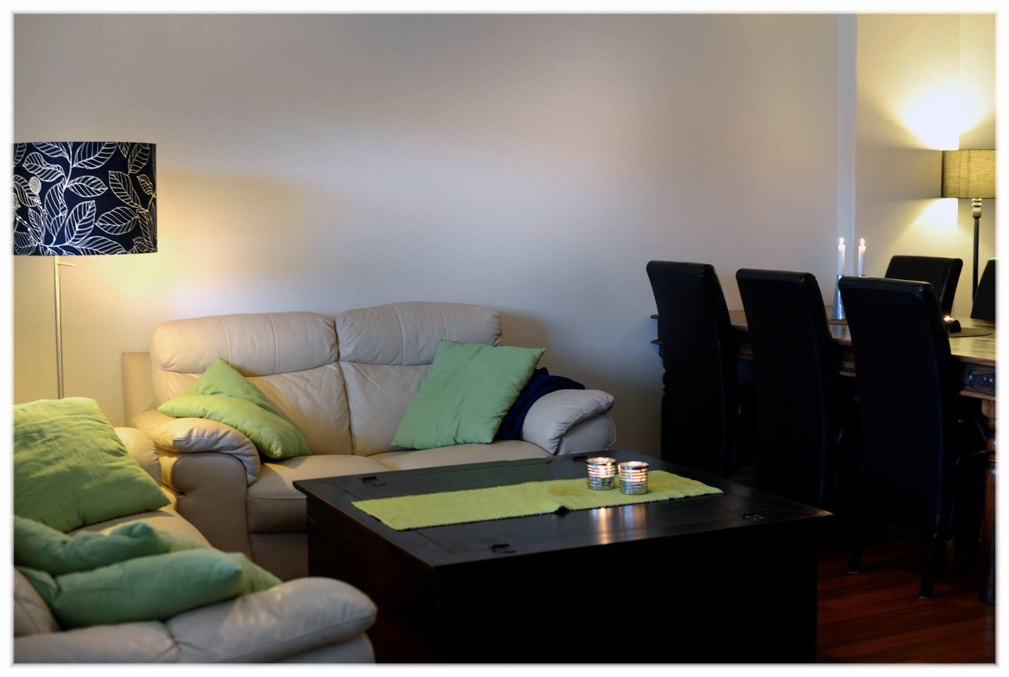 Ein Wohnzimmer mit einer Couch, zwei Sesseln, einem Couchtisch und einem Esstisch mit Stühlen.