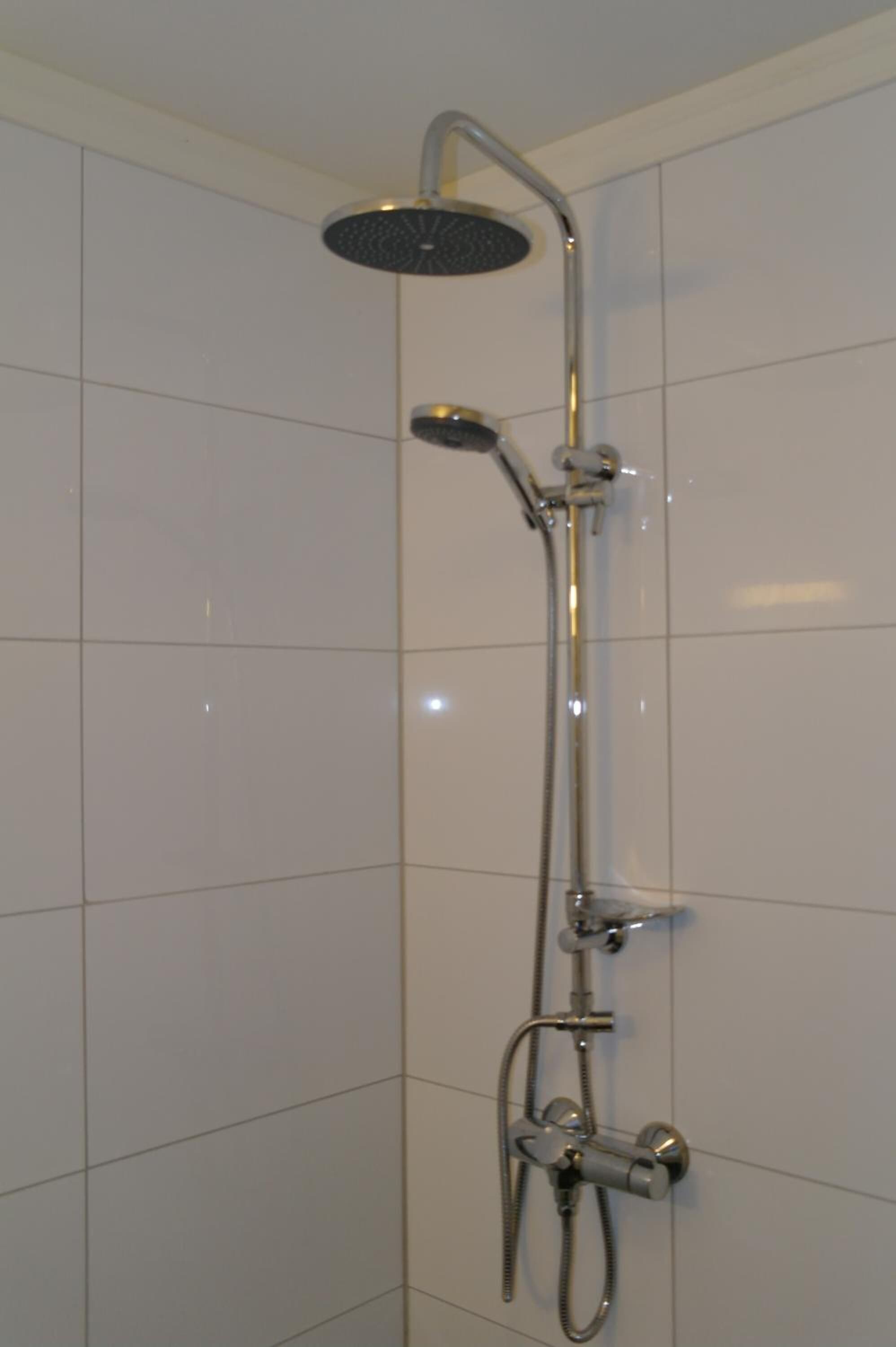 A shower with a handheld showerhead and a wall-mounted faucet.
