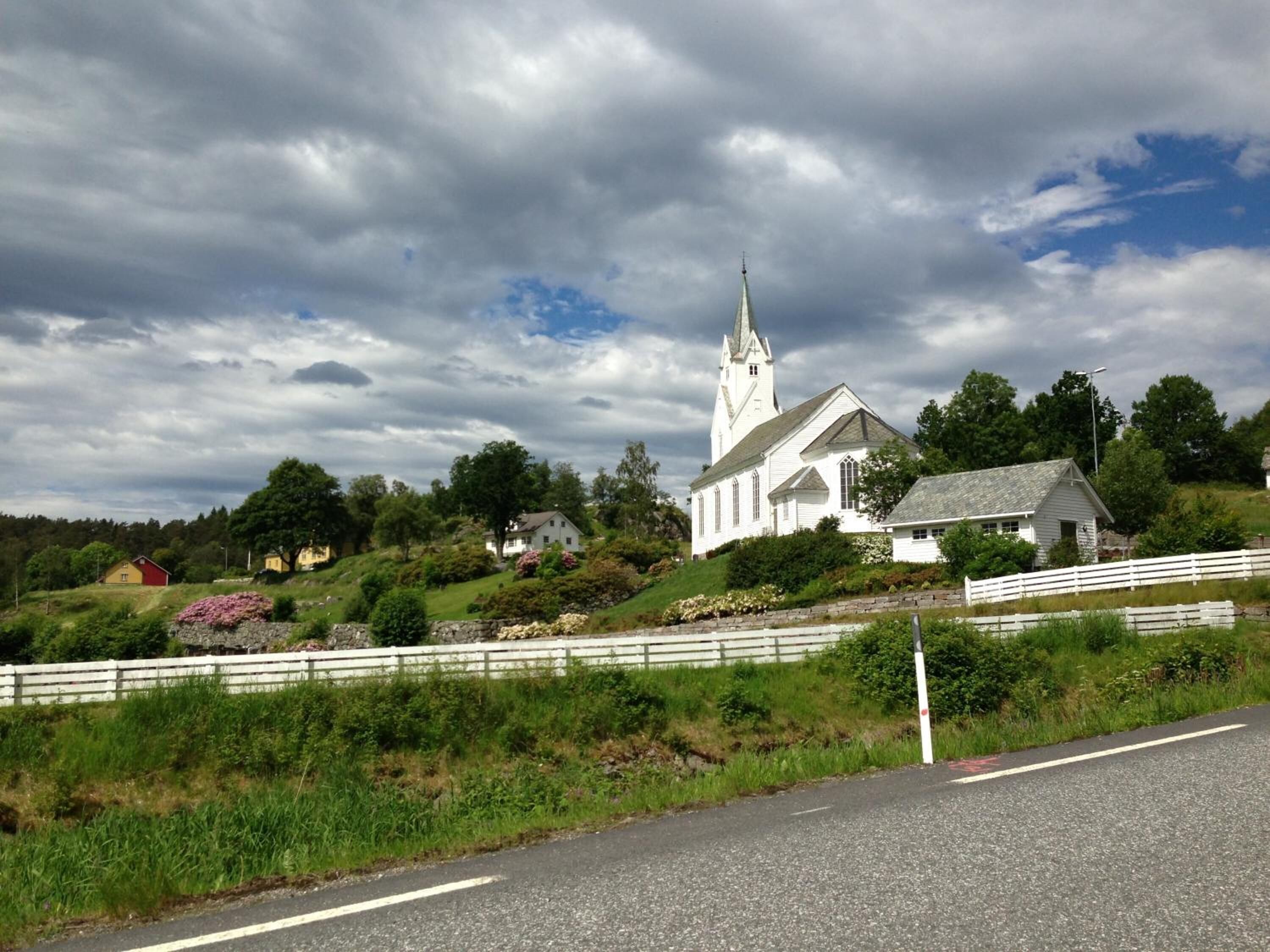 A white church with a steeple, surrounded by greenery and a white fence.