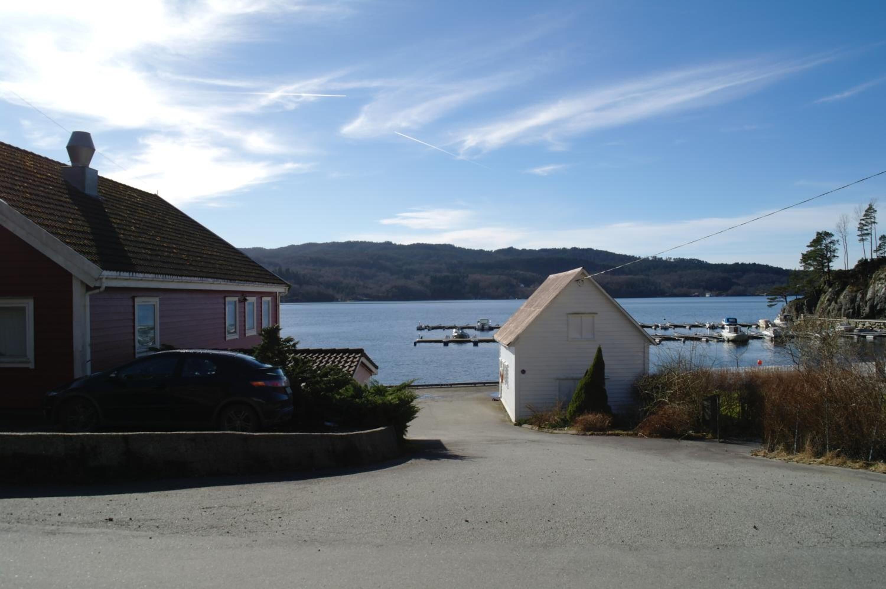 A residential area with a house, a car, and a small shed near a body of water with boats docked.