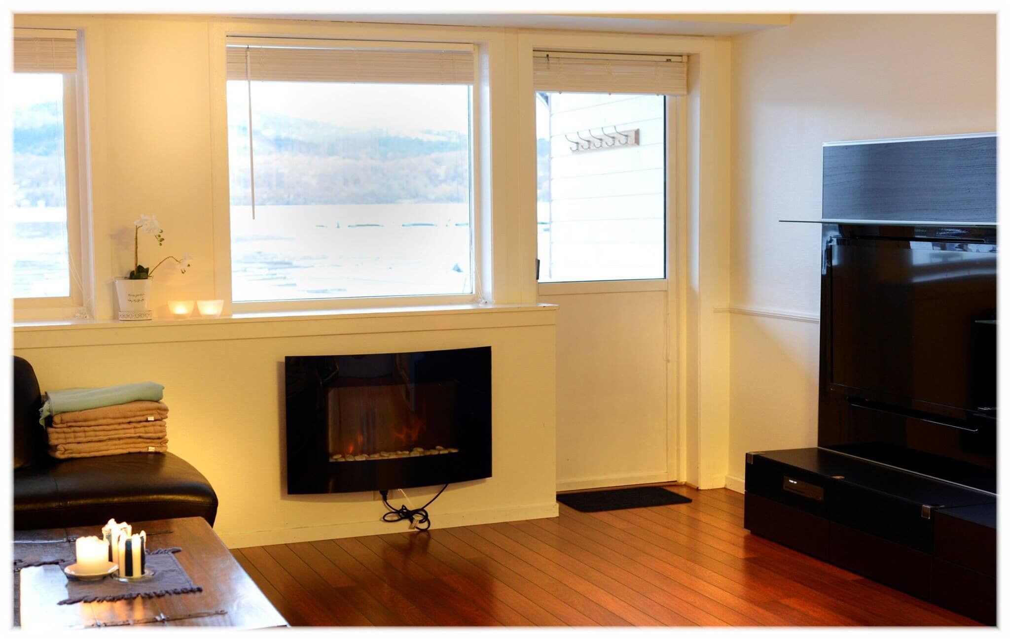 A living room with a fireplace, a television, and a view of a snowy landscape through the windows.