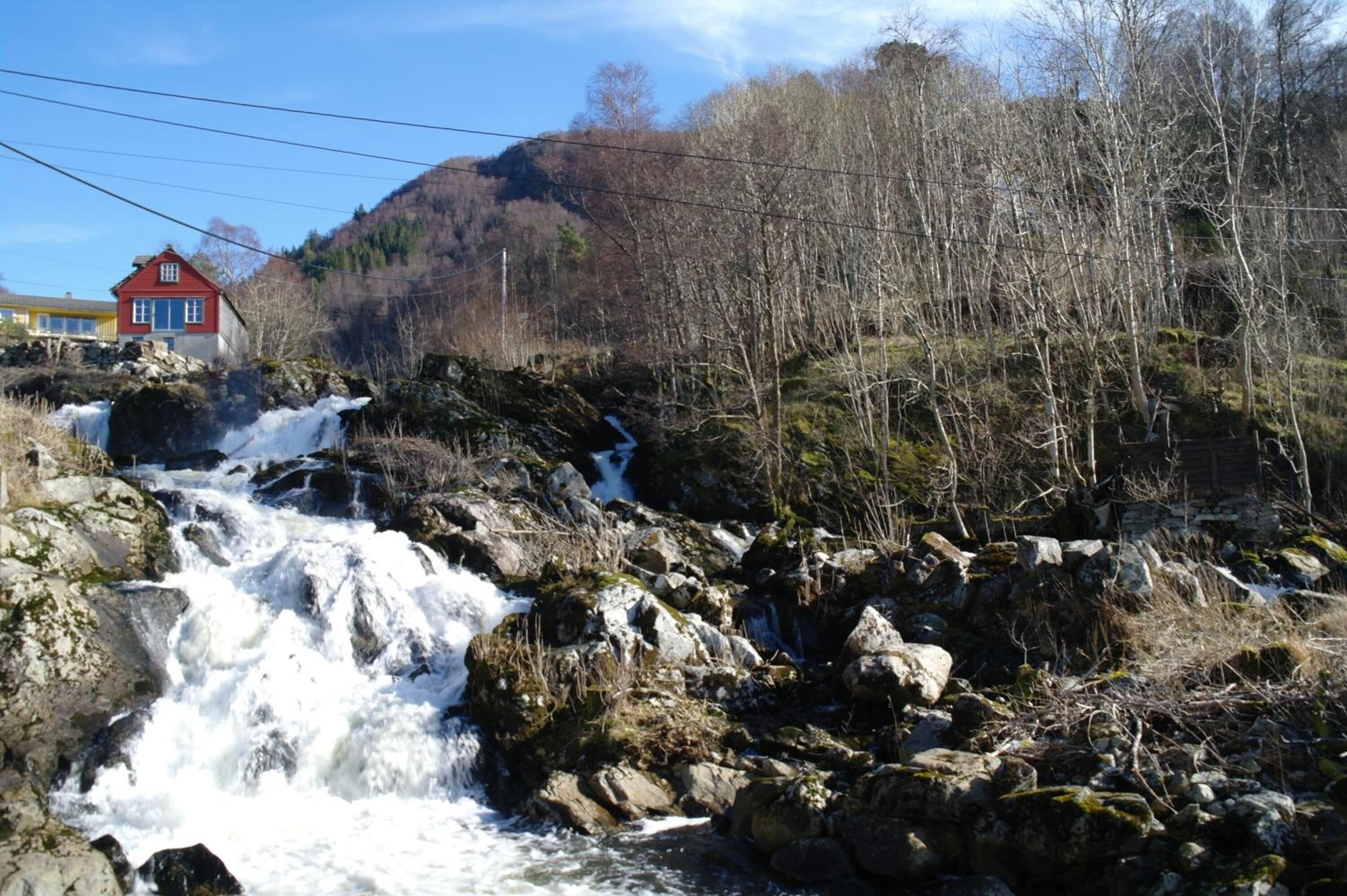 Una cascada se precipita sobre rocas, con una casa roja al fondo.