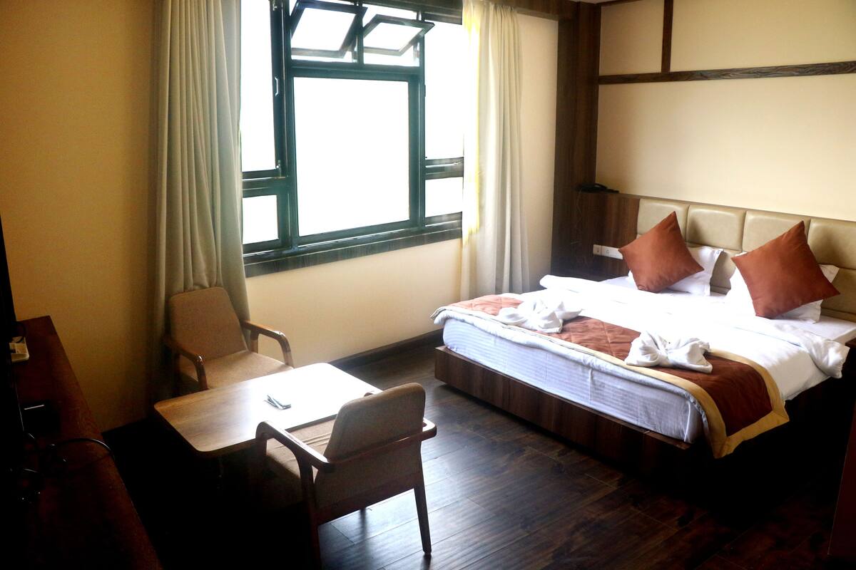 Una habitación de hotel con cama, una silla, una mesa y una ventana con cortinas.