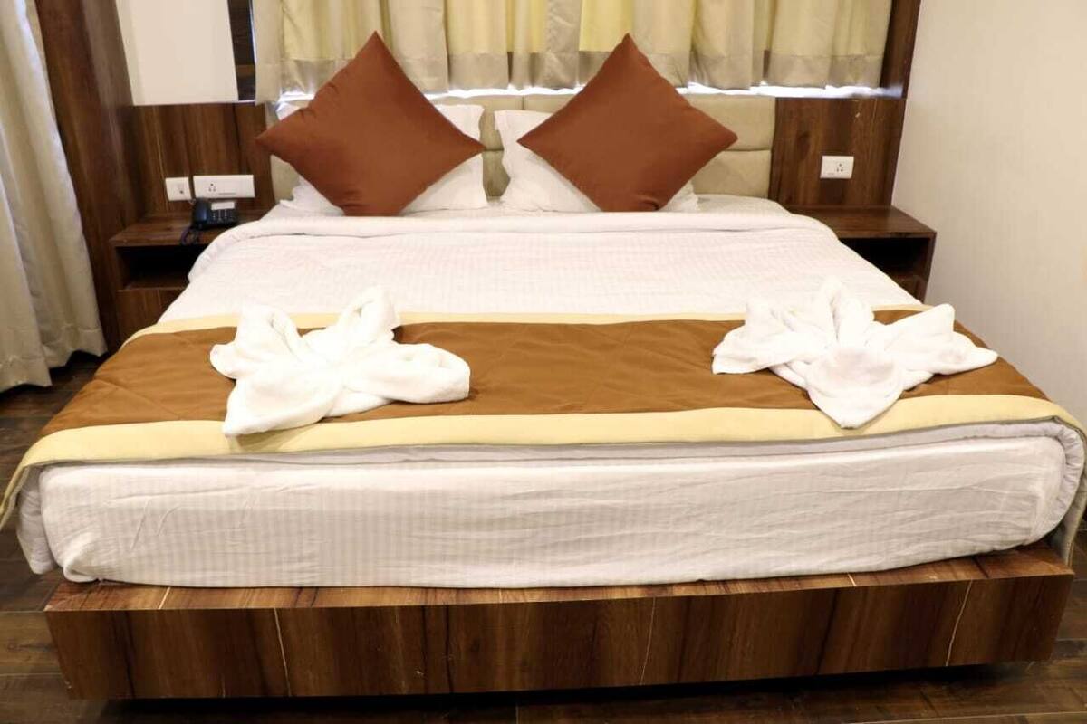 Una cama bien tendida con ropa de cama marrón y blanca, dos almohadas marrones y dos toallas blancas sobre la cama.