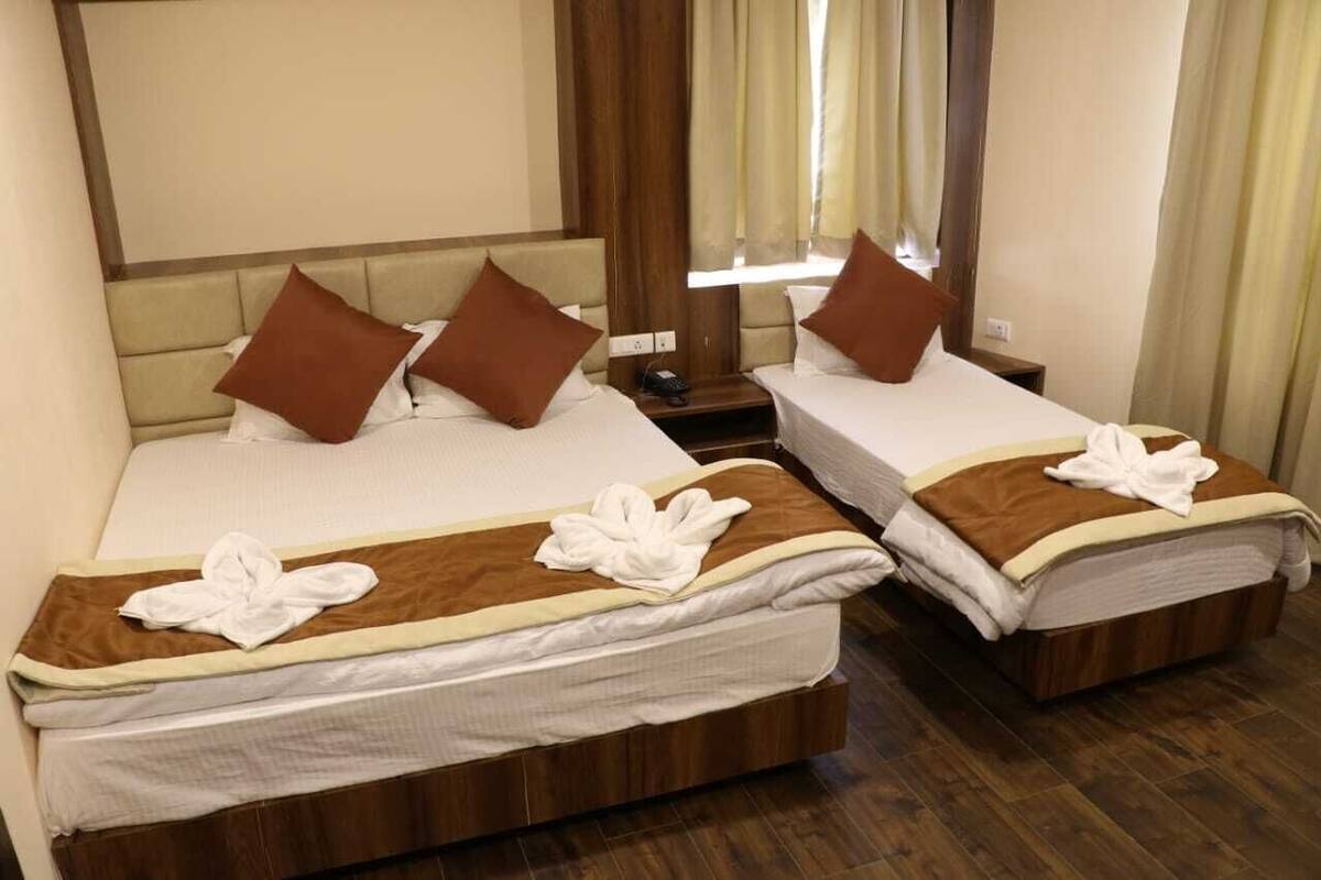 Habitación de hotel con dos camas, cada una con cabecero marrón, ropa de cama blanca y manta marrón. Entre las camas, una mesita de noche de madera con un teléfono.