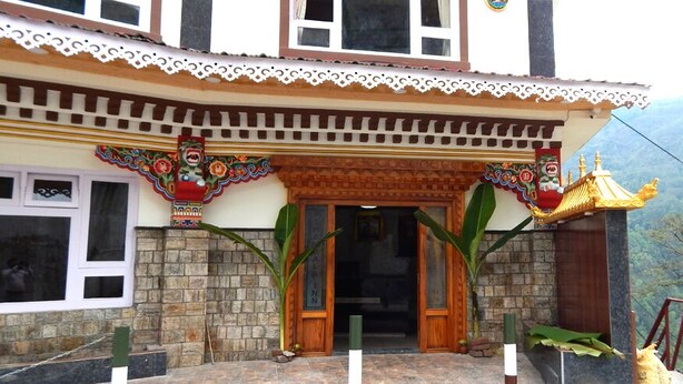 A traditional building with a wooden entrance, decorative elements, and a view of mountains in the background. - Hotel Shambala Inn (Gangtok)