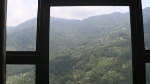 A view through a window of a mountainous landscape with scattered buildings. - Hotel Shambala Inn (Gangtok)