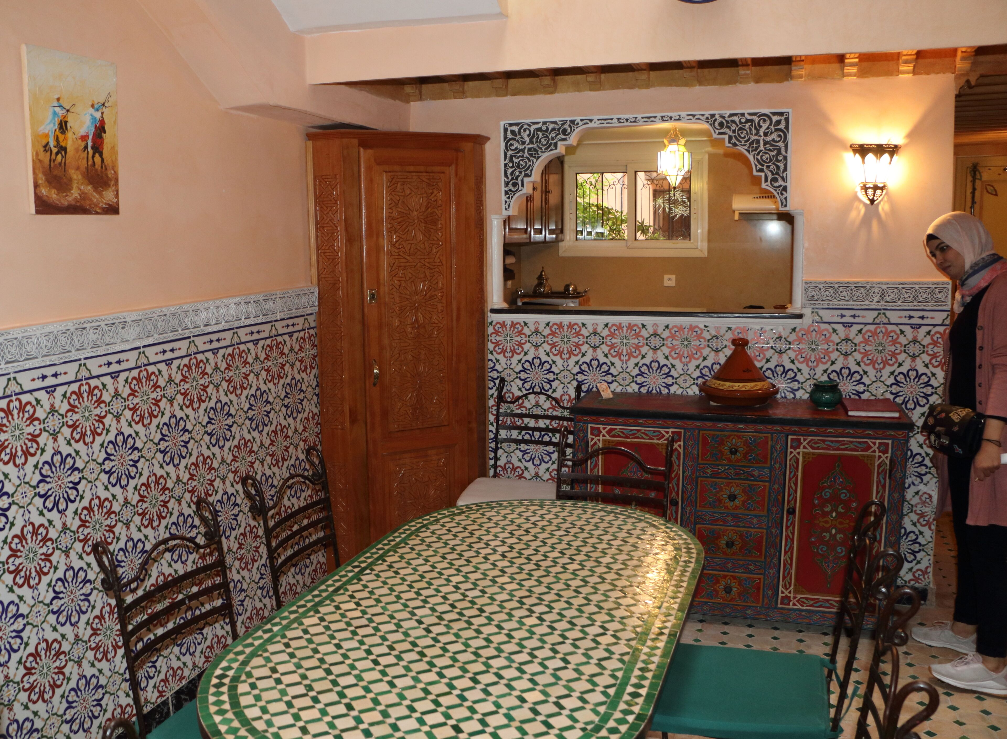 Una habitación con una mesa de comedor, sillas, un armario, un espejo y un detalle decorativo en la pared.
