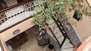 Une pièce avec un sol à motifs, une chaise verte, une petite table, un meuble décoratif et une plante suspendue.