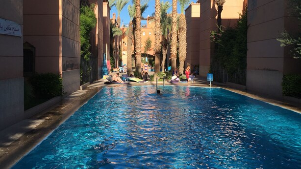 Une piscine bordée de palmiers, avec des bâtiments de chaque côté.