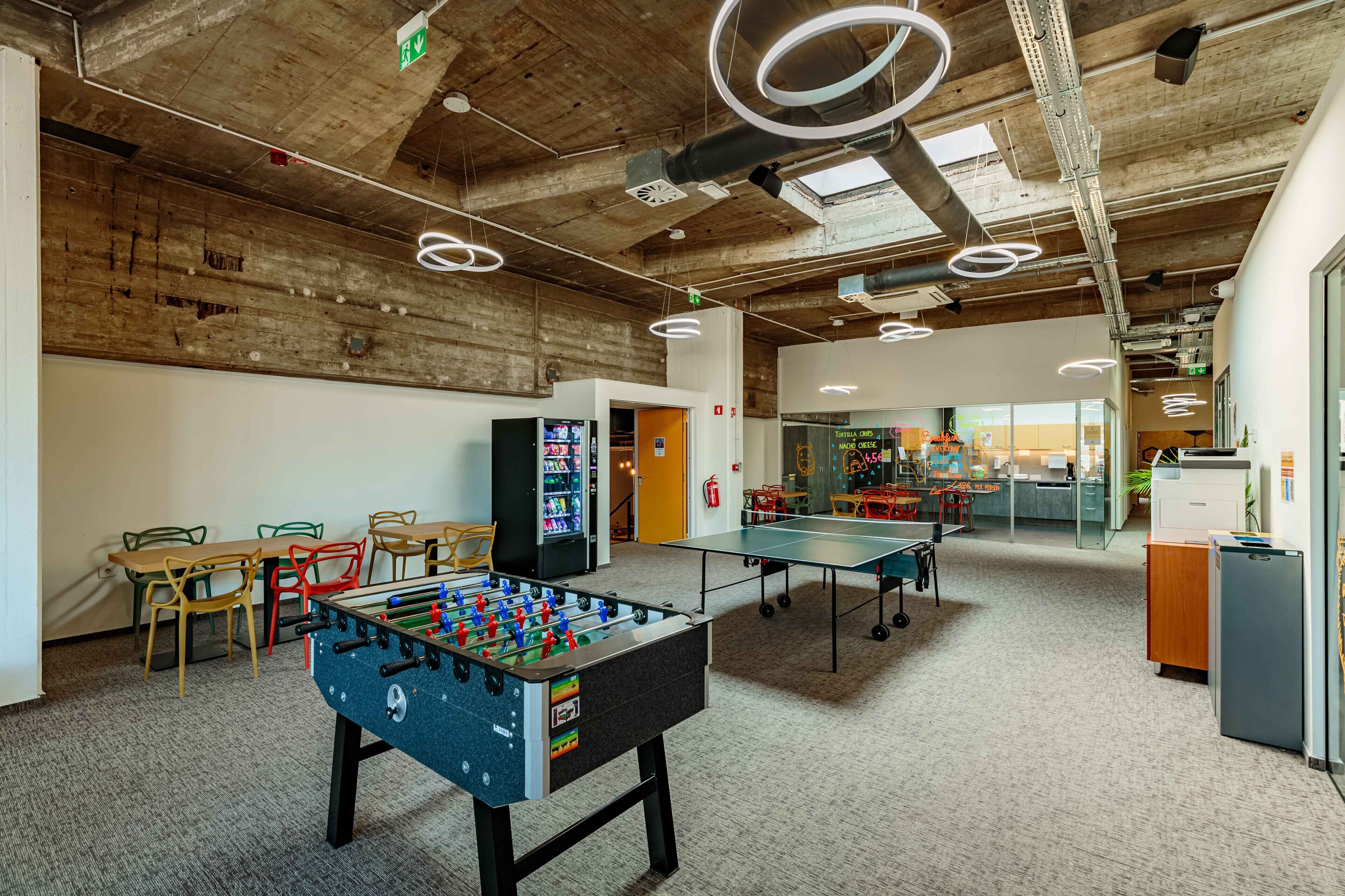 A spacious indoor area with a foosball table, ping pong table, and a vending machine.
